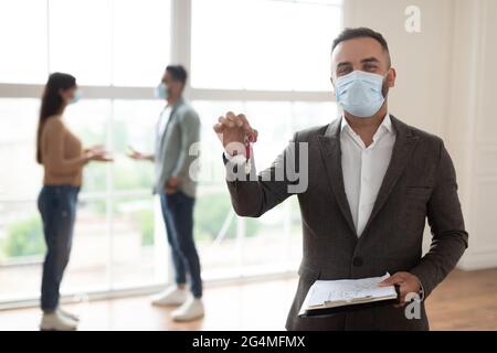 Ritratto di sorridente agente immobiliare in maschera mostrando le chiavi Foto Stock