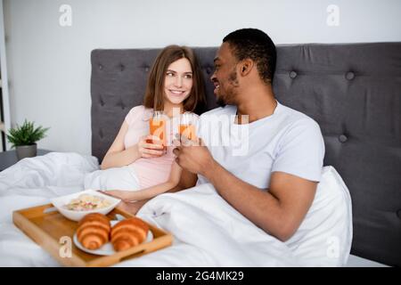 Una coppia multirazziale che ama fare colazione a letto insieme e trascorrere la luna di miele in hotel Foto Stock
