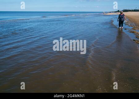 Una donna bionda di mezza età passeggiava nel mare lungo la costa della North Beach di Mablethorpe nel Lincolnshire Foto Stock