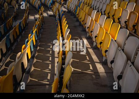 File vuote di posti a sedere in uno stadio di calcio con panchine gialle e blu Foto Stock