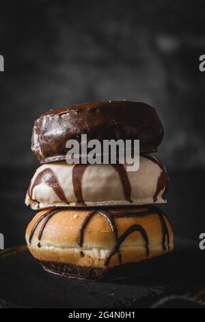 Pila di tre diverse ciambelle fresche con glassa di cioccolato e caramello su una tavola di legno Foto Stock