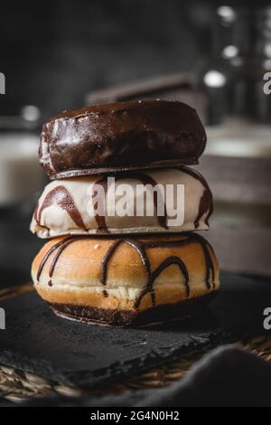 Pila di tre diverse ciambelle fresche con glassa di cioccolato e caramello su una tavola di legno Foto Stock