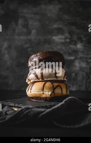 Pila di tre diverse ciambelle fresche con glassa di cioccolato e caramello su una tavola di legno Foto Stock