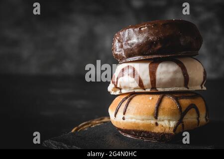 Pila di tre diverse ciambelle fresche con glassa di cioccolato e caramello su una tavola di legno Foto Stock