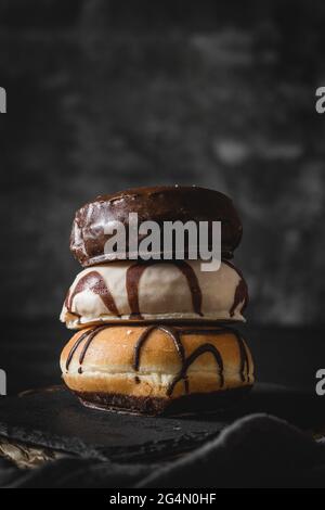 Pila di tre diverse ciambelle fresche con glassa di cioccolato e caramello su una tavola di legno Foto Stock