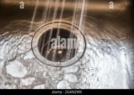 Spruzzatura di acqua monocromatica in uno smaltimento dei rifiuti in un lavello di acciaio inossidabile con acqua e bolle che si accumulano e corrono in superficie - qualche grano e momo Foto Stock