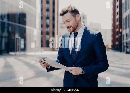 Il proprietario di affari che legge le notizie positive in giornale mentre cammina al lavoro Foto Stock