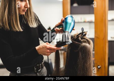 Master donna parrucchiere asciuga i capelli della ragazza con un asciugacapelli dopo il lavaggio in un salone di bellezza. Foto Stock