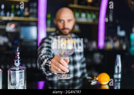 Il barista maschile offuscato e irriconoscibile serve cocktail con buccia d'arancia mentre si trova al bancone del bar moderno Foto Stock