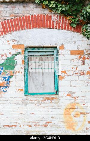 Frammento di facciata di casa in pietra con piccola finestra in legno e muro incrinato nella luce del giorno Foto Stock