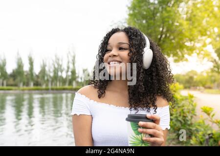 Giovane bruna felice in abiti casual firma carte su pila di scatole di cartone contro il muro grigio mentre si sposta in nuovo appartamento guardando la macchina fotografica Foto Stock