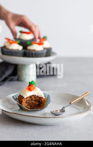 Cupcake di carote mangiato a metà con crema sul piatto contro la persona offuscata che tratta con il dessert Foto Stock