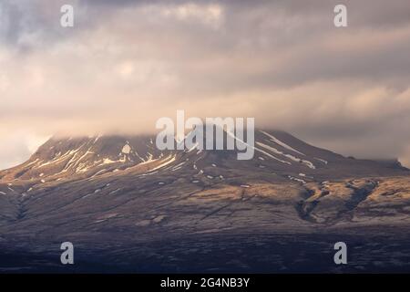 Le fitte nuvole galleggiano sul cielo del mattino sopra il crinale di montagna coperto di neve in Islanda Foto Stock