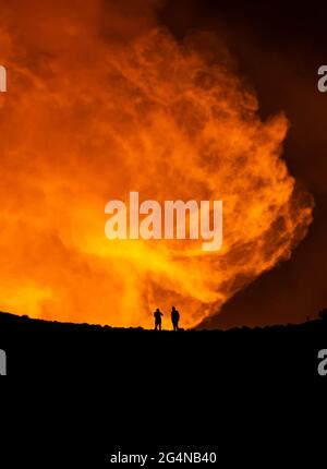 Silhouette di viaggiatori anonimi che si levano contro il profumo arancione del vulcano attivo in Islanda Foto Stock