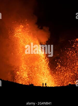 Silhouette di viaggiatori anonimi che si levano contro il profumo arancione del vulcano attivo in Islanda Foto Stock