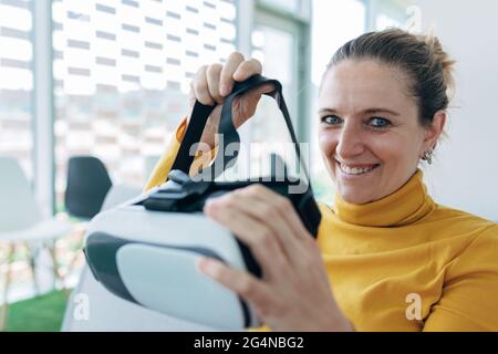 Donna in abito casual seduto sul divano e utilizzando occhiali VR vicino alle finestre in un edificio luminoso Foto Stock