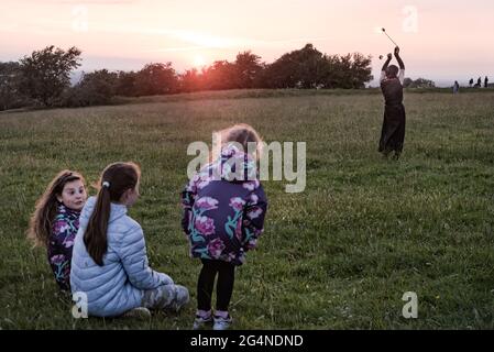 Contea di Meath, Irlanda. 21 Giugno 2021. Tre bambini piccoli guardano un giocoliere che si esibisce al tramonto. Centinaia di persone si sono riunite nella collina di Tara ieri sera per il Solstizio d'Estate del 2021. Ogni anno, la gente si riunisce sulla collina di Tara per celebrare il solstizio estivo, che è stato un luogo spirituale e storico per migliaia di anni. Credit: SOPA Images Limited/Alamy Live News Foto Stock