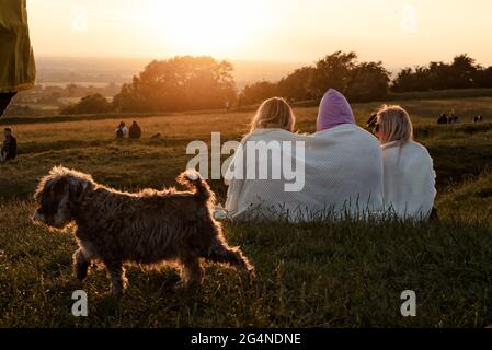 Contea di Meath, Irlanda. 21 Giugno 2021. Tre donne che si siedono e guardano il tramonto mentre un piccolo cane cammina by.centinaia di persone si sono riunite nella collina di Tara ieri sera per il Solstizio d'Estate del 2021. Ogni anno, la gente si riunisce sulla collina di Tara per celebrare il solstizio estivo, che è stato un luogo spirituale e storico per migliaia di anni. Credit: SOPA Images Limited/Alamy Live News Foto Stock