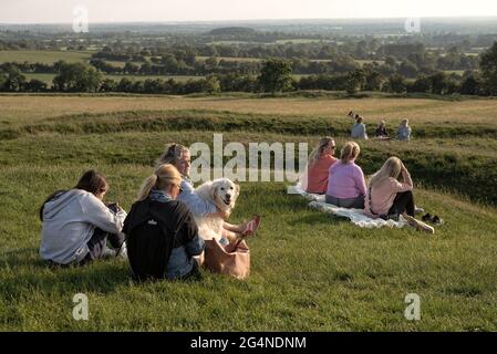 Contea di Meath, Irlanda. 21 Giugno 2021. Gruppi di persone e un cane guardare il tramonto. Centinaia di persone si sono riunite nella collina di Tara ieri sera per il Solstizio d'Estate del 2021. Ogni anno, la gente si riunisce sulla collina di Tara per celebrare il solstizio estivo, che è stato un luogo spirituale e storico per migliaia di anni. Credit: SOPA Images Limited/Alamy Live News Foto Stock