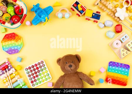 Telaio giocattolo per bambini con orsacchiotto, giocattoli in legno e musical, abacus, aereo, pop it fidget giocattoli su sfondo giallo Foto Stock