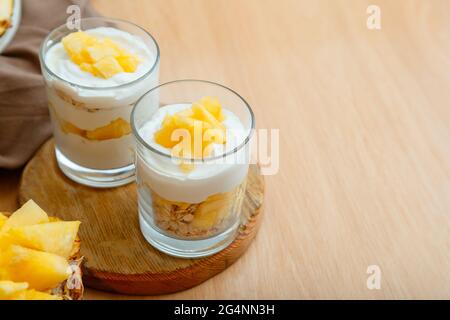 Gustosi dessert di ananas con sminuzzati di ananas fresco e succoso. Dessert per la colazione con granola di avena, yogurt greco e ananas a strati in vetro Foto Stock