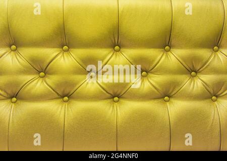 Divano con tappezzeria in pelle gialla o oro con design a tasti motivo arredamento stile decorazione texture sfondo. Foto Stock