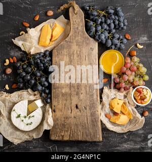 Tagliere in legno vintage vuoto al centro del telaio fatto di uva da miele formaggio snack altri ingredienti gastronomia spuntini. Simulazione dello spazio di copia o. Foto Stock