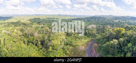 Una strada che attraversa la foresta pluviale primaria nell'Amazzonia ecuadoriana, che si affaccia sulla foresta fino a un villaggio colonico in lontananza. La costruzione della strada è la guida Foto Stock
