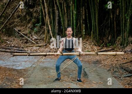 Asiatic Woman solleva un bambù in una strada asciutta a Minca, Colombia Foto Stock