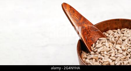 Semi di girasole sbucciati in una piccola ciotola di legno o in una tazza con cucchiaio sulla tavola bianca, spazio per il testo a sinistra Foto Stock