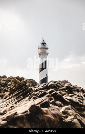 Faro dietro le rocce di Menorca, Spagna Foto Stock