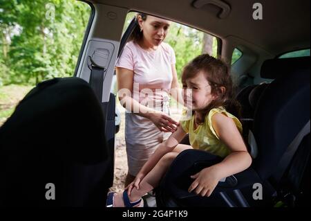 Cute baby girl piangendo quando la mamma la mette sul seggiolino per auto del bambino. Sicurezza di viaggiare in un'auto con bambini Foto Stock