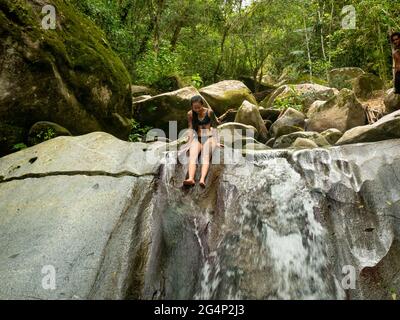 Donna asiatica al bordo della cascata del fiume, circa per saltare a Minca, Colombia Foto Stock