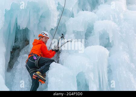 L'atleta sale sulla cascata ghiacciata, facendo oscillare l'ascia picca nel ghiaccio e usandola come grip per tirarsi in su Foto Stock