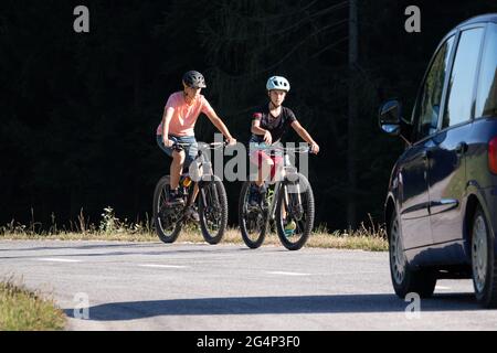 Auto e due ciclisti femminili in pericolo su una strada trafficata con auto che guida verso di loro. Foto Stock