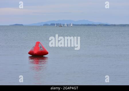 Galleggiante gonfiabile rosso su una superficie di mare calmo con gommoni a vela e imbarcazione di supporto su sfondo sfocato. Foto Stock