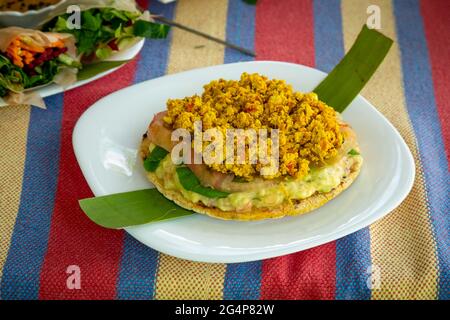 Tipico snack colombiano AREPA farcito con pomodoro, avocado e tofu servito su un piatto bianco Foto Stock