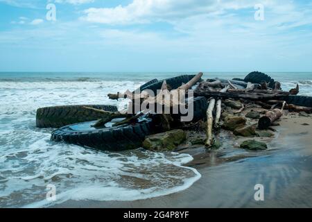 Enormi pneumatici di macchinari pesanti con enormi tronchi e pietre sulla riva della spiaggia per tagliare la forza delle onde Foto Stock