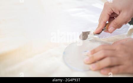 Closeup di sarti tavolo con le mani femminili tracciando tessuto con righello curva per fare un modello per abiti in officina. Foto Stock