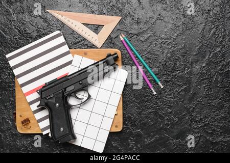 Pistola e cancelleria su sfondo scuro. Concetto di ripresa scolastica Foto Stock