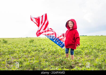 Adorabile bambina che tiene la bandiera americana all'aperto nella bella giornata estiva. USA festeggiano il 4 luglio . Concetto di giorno dell'indipendenza. Foto Stock