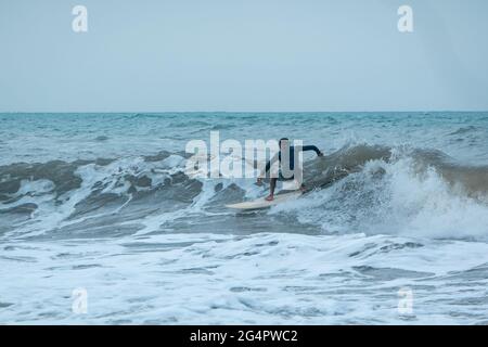 Palomino, Dibulla, la Guajira, Colombia - Maggio 24 2021: Giovani Latini Surf in the Ocean Waves at Sunset under a Cloudy Sky Foto Stock