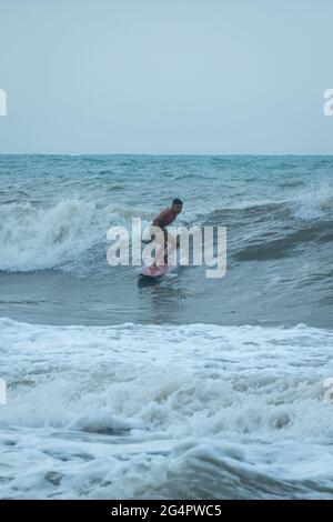 Palomino, Dibulla, la Guajira, Colombia - Maggio 24 2021: Giovani Latini Surf in the Ocean Waves at Sunset under a Cloudy Sky Foto Stock