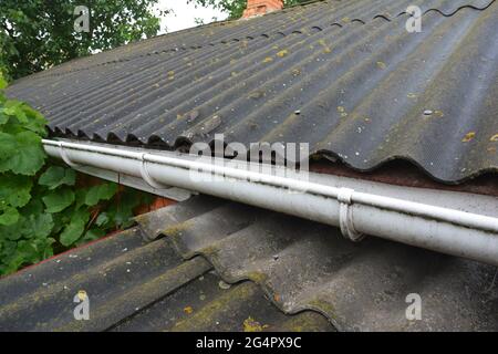 Un primo piano di un tetto in amianto con un grondaia in plastica. Un vecchio tetto di amianto corrugato. Foto Stock