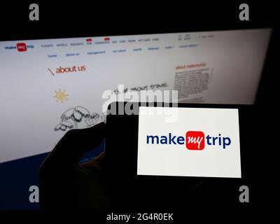 Persona che tiene il cellulare con il logo della società indiana di viaggi online MakeMyTrip Ltd sullo schermo di fronte alla pagina web aziendale. Mettere a fuoco il display del telefono. Foto Stock