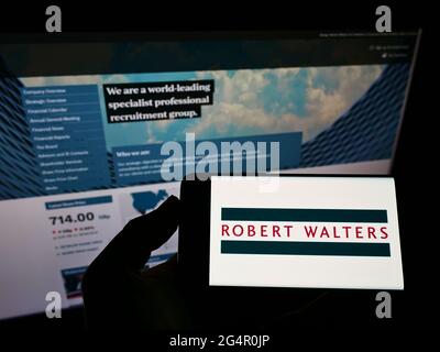 Persona che tiene il cellulare con il logo della società di reclutamento inglese Robert Walters plc sullo schermo di fronte alla pagina web aziendale. Mettere a fuoco il display del telefono. Foto Stock