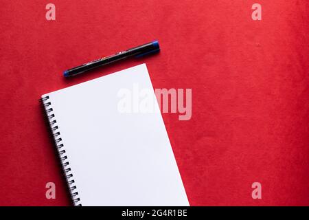 Un quaderno di carta bianca con un pennarello posizionato su uno sfondo rosso Foto Stock
