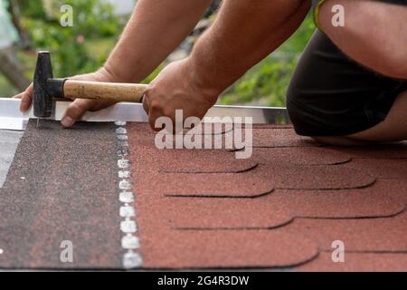 Mani di lavoro che installano le alette del tetto bituminose Foto Stock