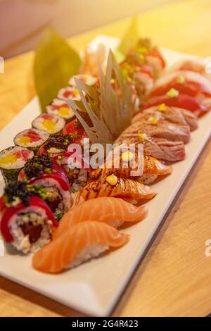 Cucina giapponese. Sushi assortito su un piatto bianco su sfondo di legno. Foto Stock