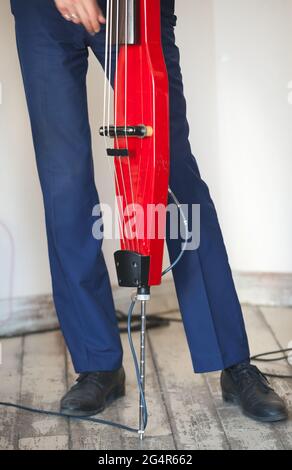 Un uomo suona il contrabbasso elettrico rosso in studio musicale, primo piano verticale con messa a fuoco selettiva. Sottofondo musicale dal vivo Foto Stock